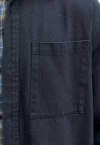 Close-up van een donkerblauwe jaszak over een blauw-gele geruite overhemdstof.