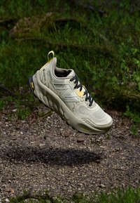 Beige terrengløpesko med mesh-overdel, svarte lisser, gule detaljer og teksturert såle. Har Gore-Tex for vannmotstand.