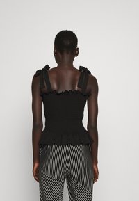 Musta smockattu yläosa, jossa on rypytetty reuna ja säädettävät nauhat, yhdistettynä mustavalkoisiin raidoitettuihin leveälahkeisiin housuihin, joissa on vinosaumat.