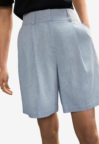 Pantaloni corti azzurro chiaro su misura realizzati in tessuto testurizzato, con pieghe frontali piatte e tasche laterali, con un taglio pulito e dritto all'orlo.