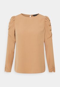 Blusa a maniche lunghe in tessuto color tan chiaro, con scollatura rotonda, spalle a palloncino e dettagli arricciati sui polsini. Chiusura a chiave sul retro.