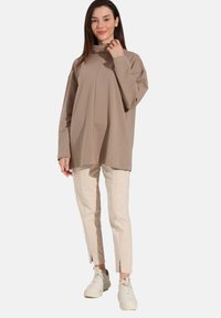 Beige oversized sweatshirt met een hoge kraag en verlaagde schouders, gecombineerd met lichtbeige tapered broek en witte sneakers.