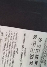 Étiquette de soin des vêtements avec des symboles de lavage incluant pas d'eau de javel, repassage à basse température, pas de séchage en tambour et instructions pour un lavage délicat en machine.
