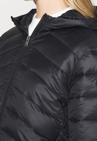 Doudoune noire avec capuche, dotée d'une fermeture éclair, d'un design matelassé et d'une texture lisse et brillante. Accentuée par une fermeture éclair argentée.
