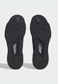 Suelas de zapato deportivo negro con patrones de agarre texturizados, que presentan una sección de acento translúcida con puntos incrustados para mejorar la tracción.