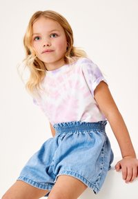 Pastellroosa ja-lilla toonides puuvillane tie-dye T-särk, millele on sobitatud helesinised teksapüksid, millel on hõlbustatud vöökoht ja mugav lõige.