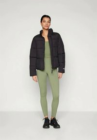 Svart puffjakke med en kort design, med horisontal søm. Kombinert med olivengrønne leggings og svarte joggesko.