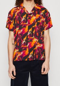 Lyhythihainen paita, jossa on musta pohja, ja siinä on abstrakti kuvio eloisan oranssin, vaaleanpunaisen ja purppuran sävyissä. Napitettava malli, jossa on tasku.