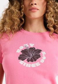 Pink cotton t-shirt featuring a black hibiscus graphic with the text "ROXY SINCE 1995" in white, round, and bold font.