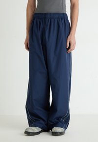 Navy waterproof pants with an elastic waistband, wide legs, and reflective side stitching. Worn over gray top and gray footwear.