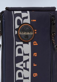 Borsa in tessuto blu navy con testo bold bianco e arancione e una toppa nera rotonda etichettata "Napapijri". Include una zip e dettagli testurizzati.
