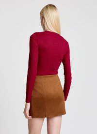 Long-sleeve ribbed top in deep red paired with a brown faux suede mini skirt, featuring a smooth texture and clean, simple lines.