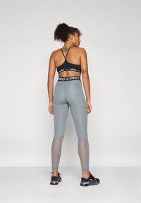 Sort sportsbh med tynde stropper; grå leggings med mesh-paneler og en struktureret finish; parret med sorte atletiske sko.