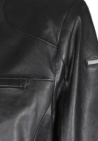 Musta nahkatakki, jossa on sileä pinta, yksityiskohtaista ompelua ja tyylikäs muotoilu, jossa olkapäällä pieni logokoriste.