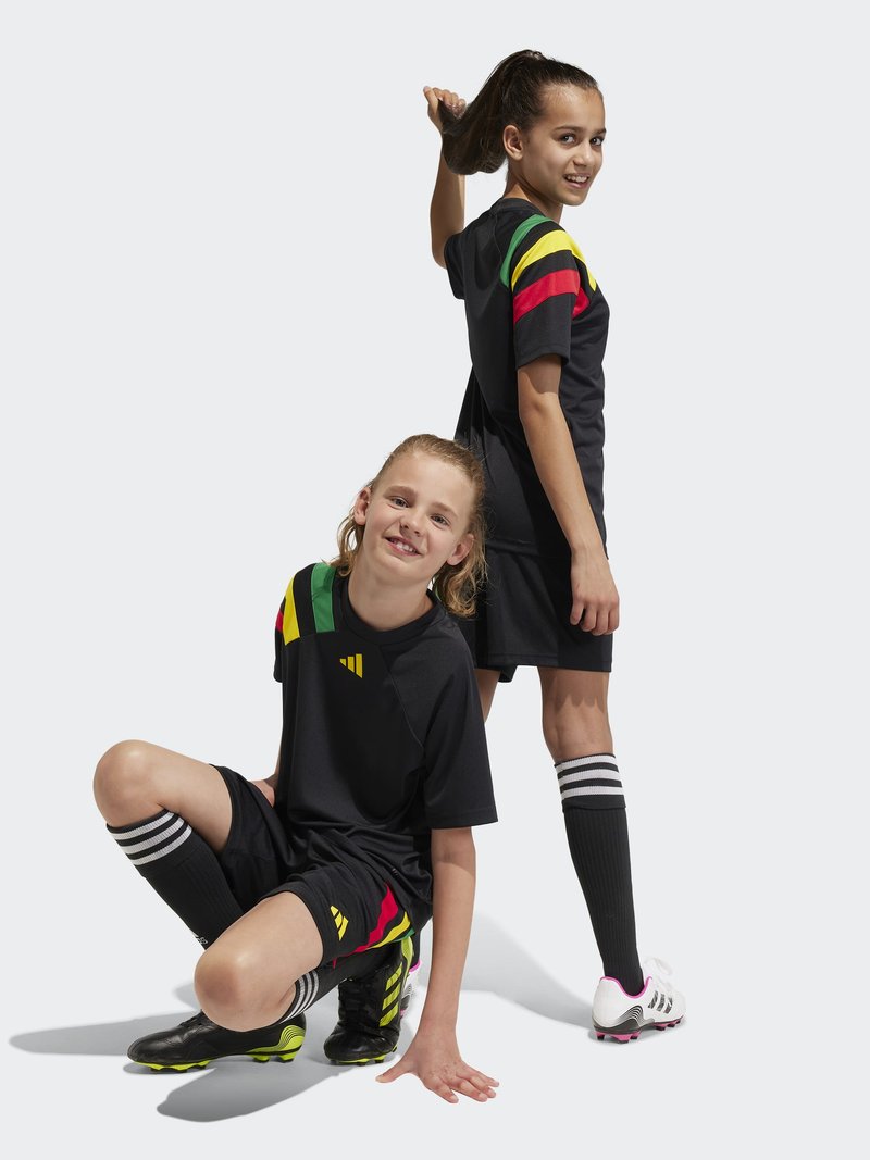 Schwarze Fußballtrikots mit bunten gestreiften Akzenten in Grün, Gelb und Rot. Die Kleidung umfasst schwarze Shorts und knielange gestreifte Socken.