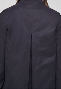 Granatowy wodoodporny płaszcz trench z gładką fakturą, wyposażony w tylny wentyl, widoczne szwy oraz kołnierz.