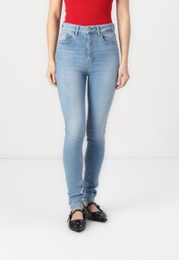 Jeans de tiro alto en azul claro con cinco bolsillos, costuras a contraste y un corte ajustado. Combinados con bailarinas negras con acentos plateados.