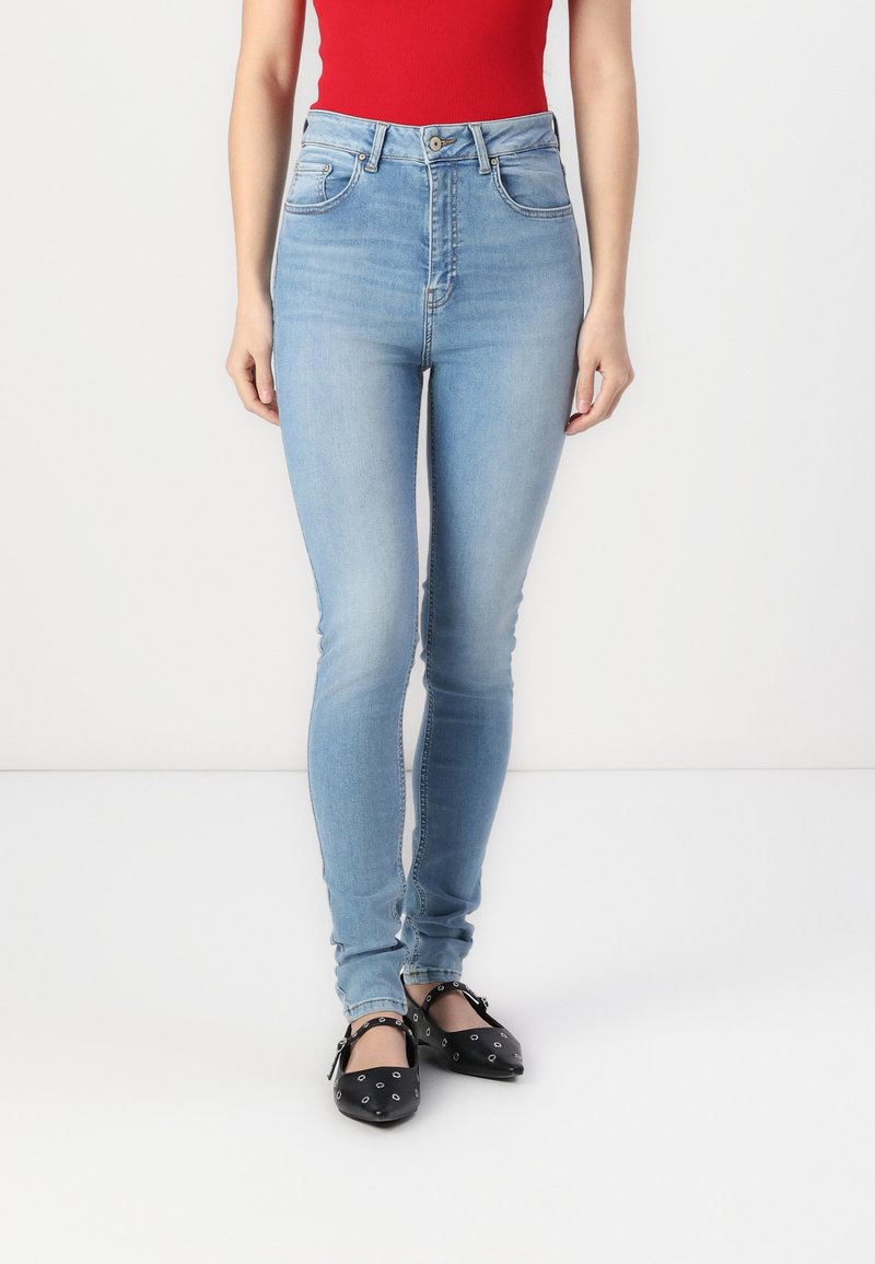 Jeans de tiro alto en azul claro con cinco bolsillos, costuras a contraste y un corte ajustado. Combinados con bailarinas negras con acentos plateados.