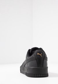 Chaussure de sport en cuir noir avec accents texturés, col rembourré et semelle en caoutchouc. Perçoit un petit logo Puma doré au talon.