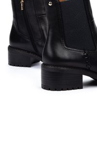 Bottines en cuir noir avec des panneaux élastiques sur les côtés, des surfaces texturées, un bout rond et un petit talon carré. Détail de fermeture éclair dorée sur un côté.