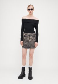 Svart ribbestrikket topp uten skuldre kombinert med et falmet svart denimskjørt med lett slitasje. Svart kraftig hælboots fullfører antrekket.