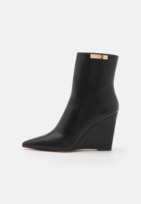 Black ankle boot with pointed toe, wedge heel, and gold "Twinset Milano" logo plaque near the top edge.