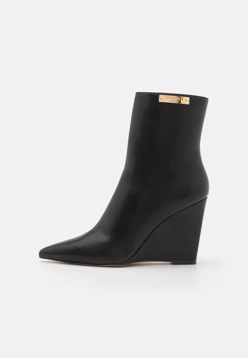 Black ankle boot with pointed toe, wedge heel, and gold "Twinset Milano" logo plaque near the top edge.