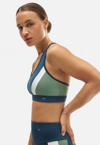 Sujetador deportivo con un diseño a bloques de color en azul oscuro, verde claro y blanco. Hecho de material elástico con una forma ajustada y detalle del logo.