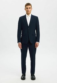 Marinblå skräddarsydd kostym med enbladsblazer, vit skjorta och svarta skor. Slät textur med slim-fit design och rena linjer.