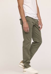 Pantalons vert olive en tissu mélangé coton, coupe droite, avec plusieurs poches, stylés avec des baskets blanches et un simple t-shirt blanc.