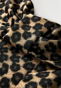 Lauka audums ar leoparda rakstu, kurā redzams strukturēts melns zieds uz zelta fona, ar maigām krokām, kas atklāj tā vieglo struktūru.