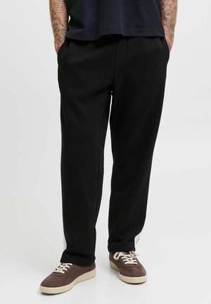 Black sweatpants with a relaxed fit, made of smooth fabric, featuring side pockets and a subtle white logo detail along the hem.