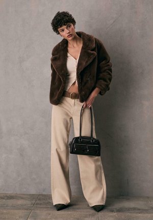 Brun faux fur jakke over en creme ribbet top, beige vidde bukser og en sort taske med dobbelte lommer og korte håndtag.