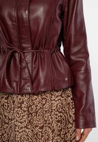 Bordeaux leren jas met een getailleerde taille, lange mouwen en een gladde textuur, gecombineerd met een gemarmerde bruine rok met bloemmotieven.
