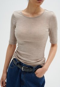 Beige těsný top s krátkým rukávem a kulatým výstřihem, v kombinaci s tmavě modrými džínami s vysokým pasem a černým opaskem se stříbrnou sponou.