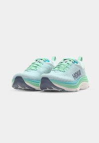 Light blue running shoes with a textured mesh upper, green accents, and a thick white and blue sole featuring a ribbed pattern.
