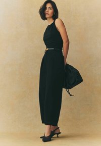 Top nero senza maniche abbinato a pantaloni neri a vita alta, stretto con una cintura marrone chiaro e nera. Borsa nera e scarpe con tacco a punta.