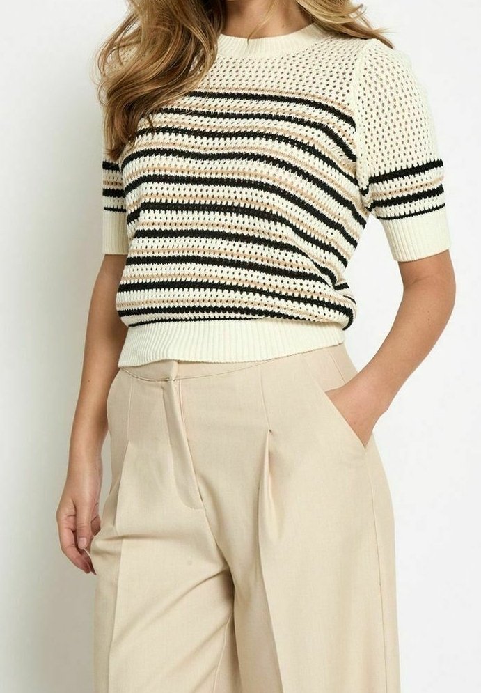 Femme portant un pull en maille crème à manches courtes avec des rayures horizontales noires et beiges, assorti à un pantalon beige taille haute.