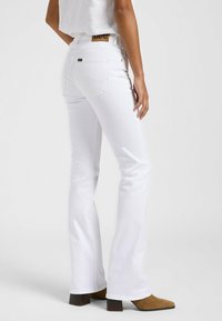 Vaqueros acampanados blancos de denim, con ligero stretch, bolsillos traseros y una etiqueta de parche de cuero en la cintura.