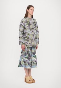 Blumendruck-Übergröße-Jacke in verschiedenen Grüntönen und Lila, kombiniert mit einem passenden Rock. Voluminöse beigen Holz-Plateauschuhe.
