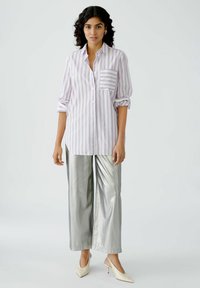 Light purple and white striped button-up shirt with a chest pocket, paired with shiny silver wide-leg pants and white heeled shoes.