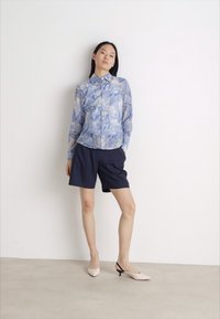 Light blue floral button-up shirt, navy shorts, and nude heeled shoes. The shirt features a soft, sheer texture with pastel floral patterns.
