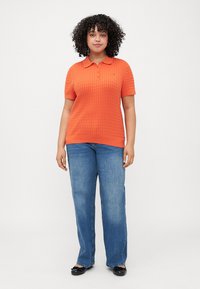  Oranje korte mouwen polo met een gestructureerd patroon, gecombineerd met blauwe rechte jeans en zwarte ballerina's.