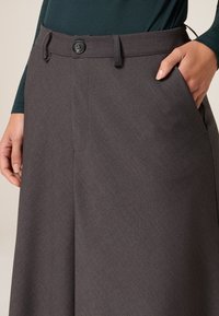Graue maßgeschneiderte Hose mit glatter Textur, weitem Beinform, frontalen Taschen und einem Knopfverschluss an der Taille.