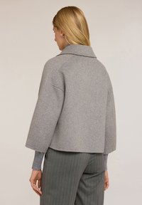 Giacca in misto lana grigia con un ampio colletto, design accorciato e spalle cadenti. Presenta polsini elastici e una trama liscia.