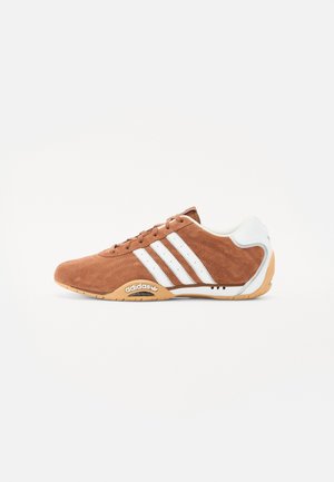 Baskets Adidas en daim marron avec des bandes blanches, un détail blanc au talon, une semelle en gomme et le logo Adidas sur le côté de la semelle.