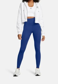 Niebieskie legginsy z wysokim stanem z elastycznego materiału, w połączeniu z białym krótkim sweatshirtem. Całość dopełniają sportowe buty.