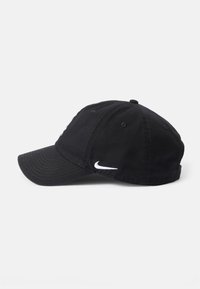Melna kokvilnas beisbola cepure ar izliekto vizu līniju, kurai sānos ir balts Nike logotips un izšuvuma detaļas uz galvas daļas.