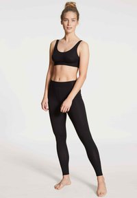 Zwarte aangesloten leggings en een bijpassende sportbeha, beide gemaakt van gladde stof met een naadloos ontwerp, getoond op een model met een neutrale achtergrond.