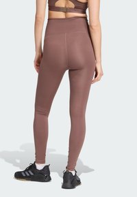 Leggings taille haute, ajustés en tissu mauve doux avec une texture lisse, associés à des chaussures de sport noires et un haut dos nageur.